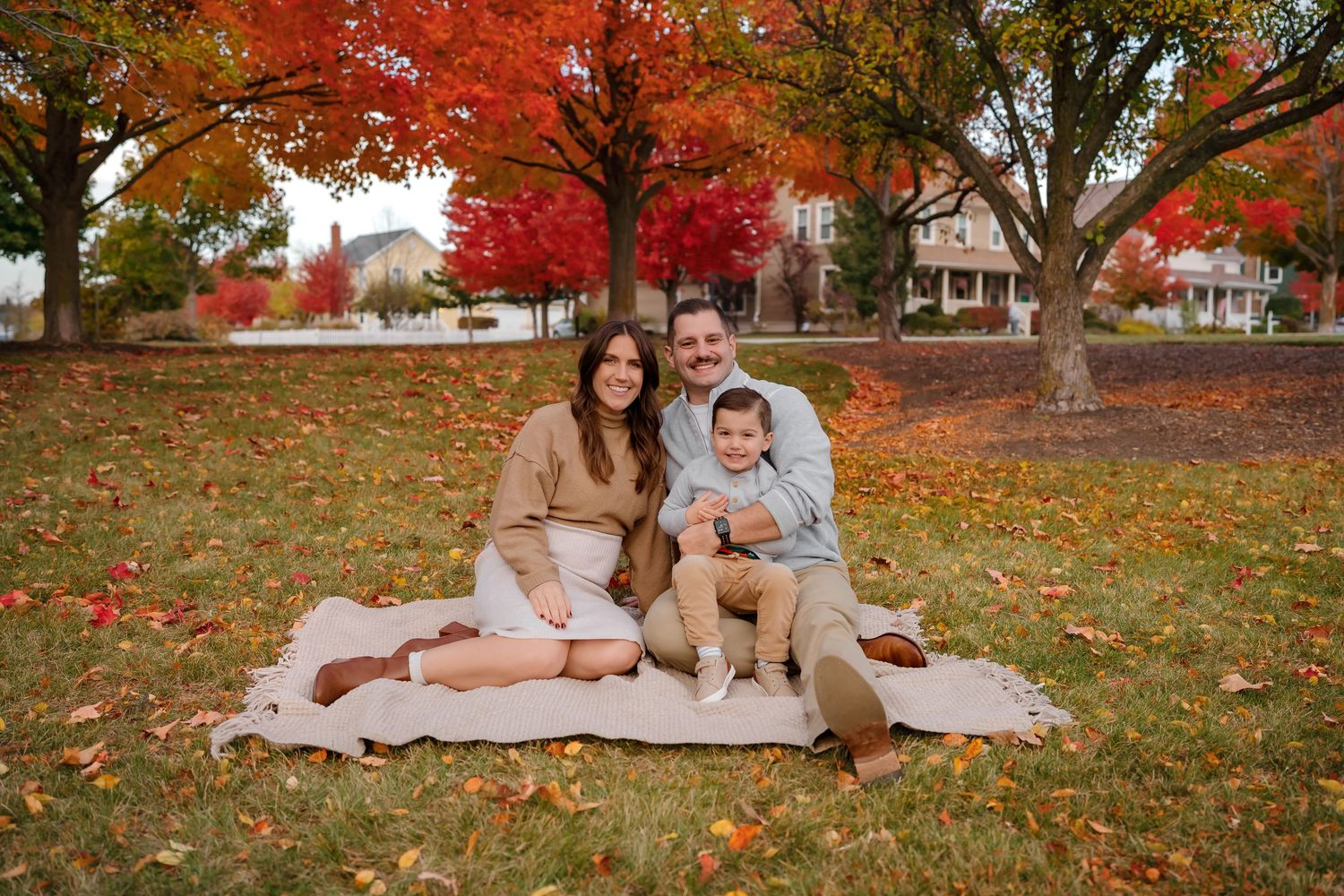 Family enjoying autumn day on blanket surrounded by vibrant red maple trees and fallen leaves.