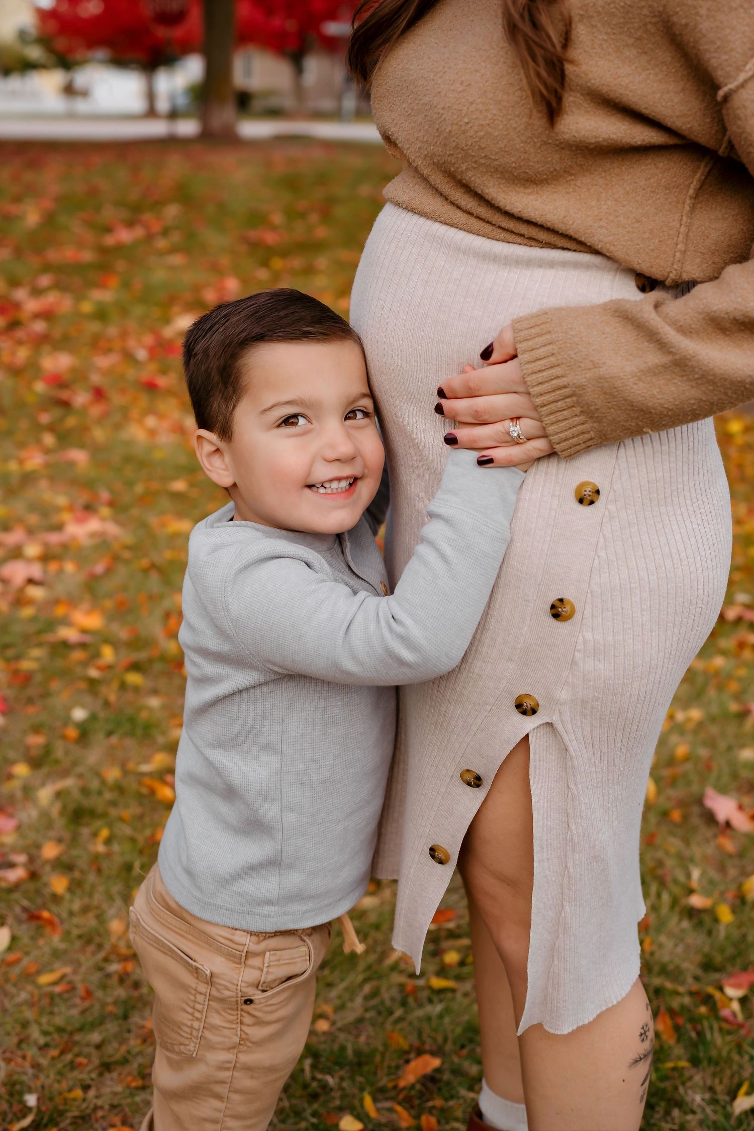 A touching family moment captured in fall as a small child hugs a parent's legs among scattered leaves.