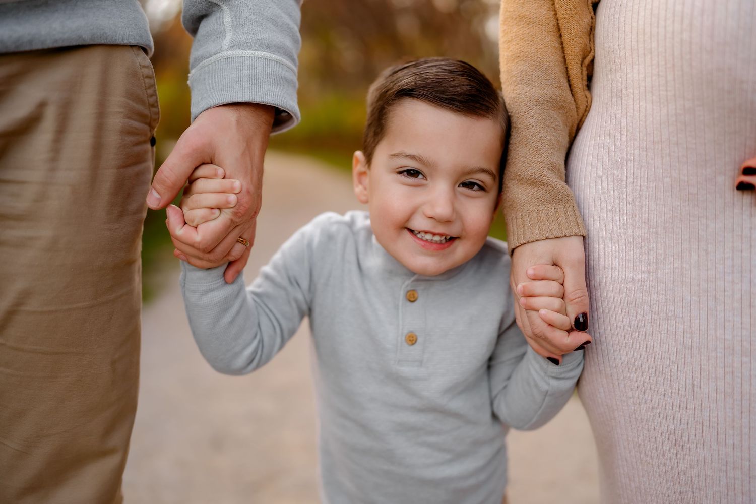 A small child in a light gray sweater holds hands with an adult while walking outdoors.