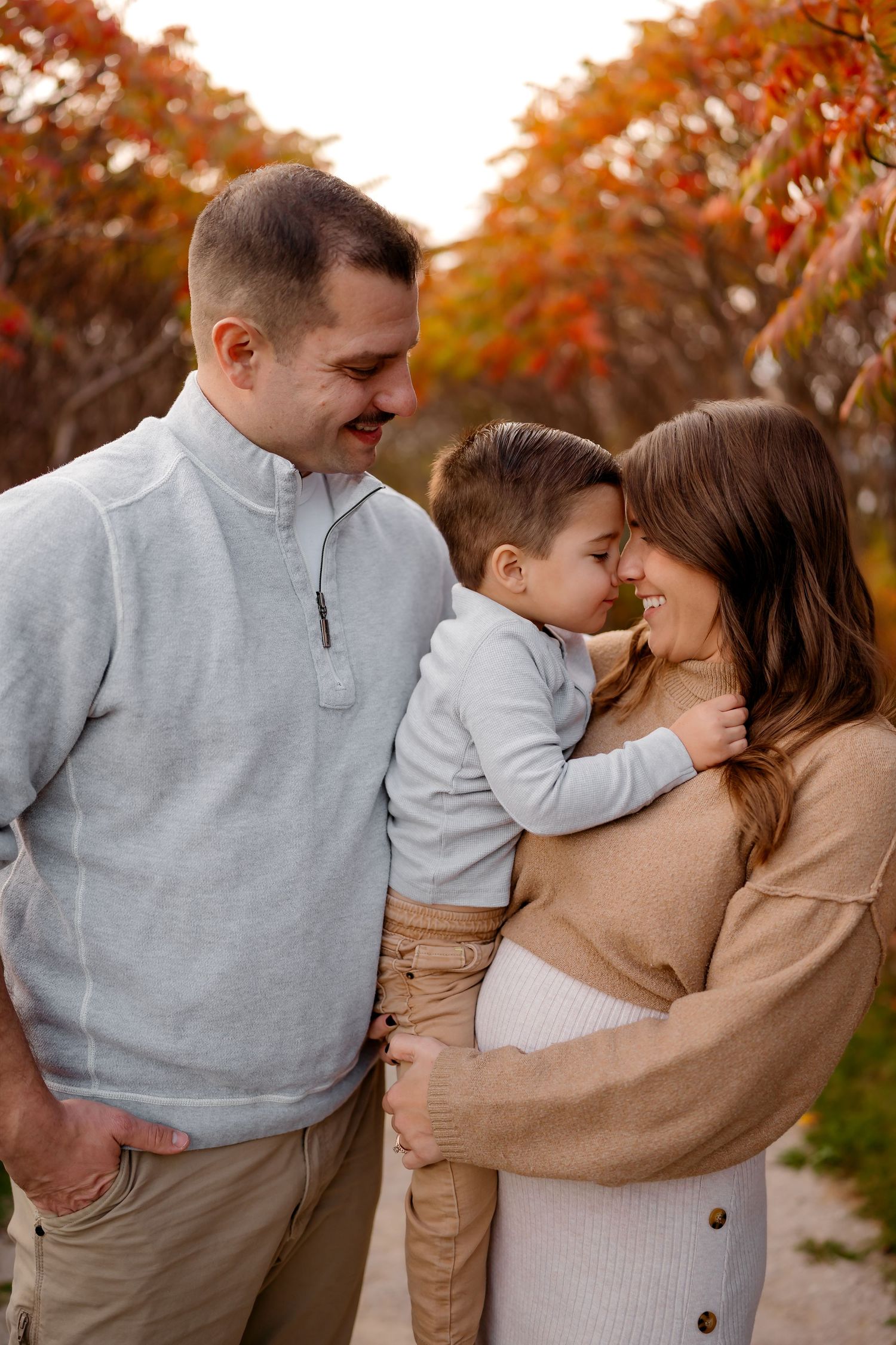 A family shares tender moments together against a backdrop of autumn trees with orange foliage.