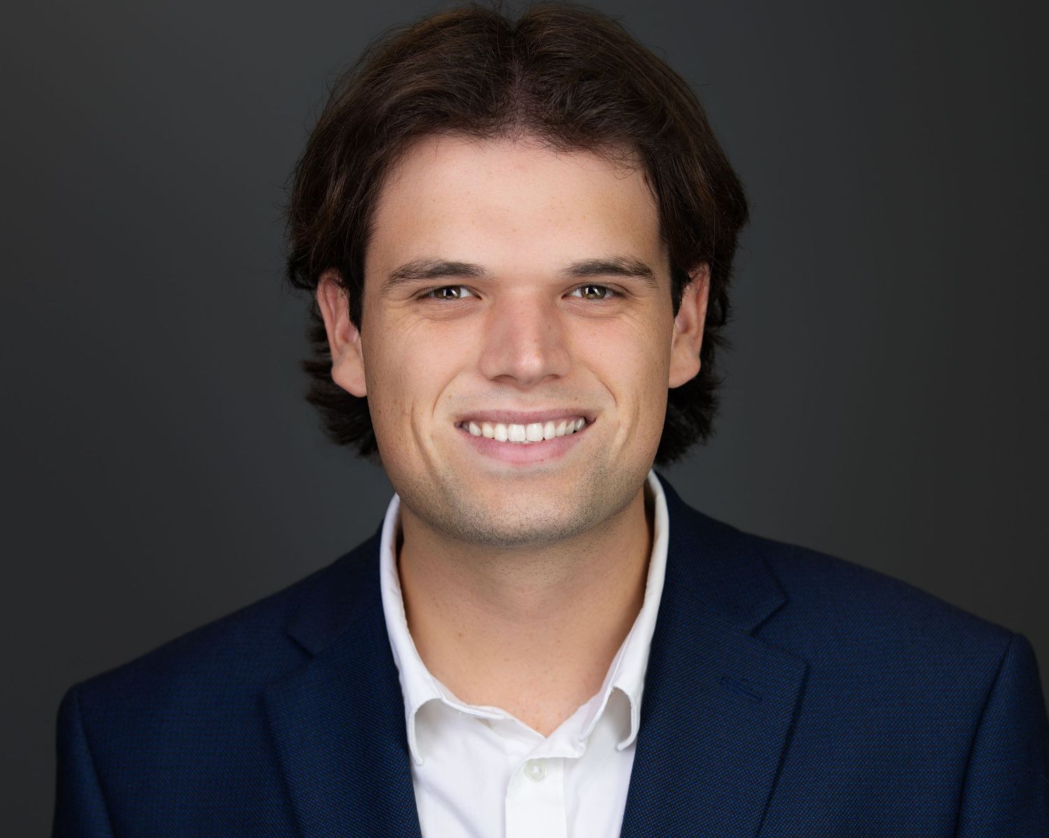 Professional headshot of a person in glasses and white medical coat with purple shirt smiling at the camera.