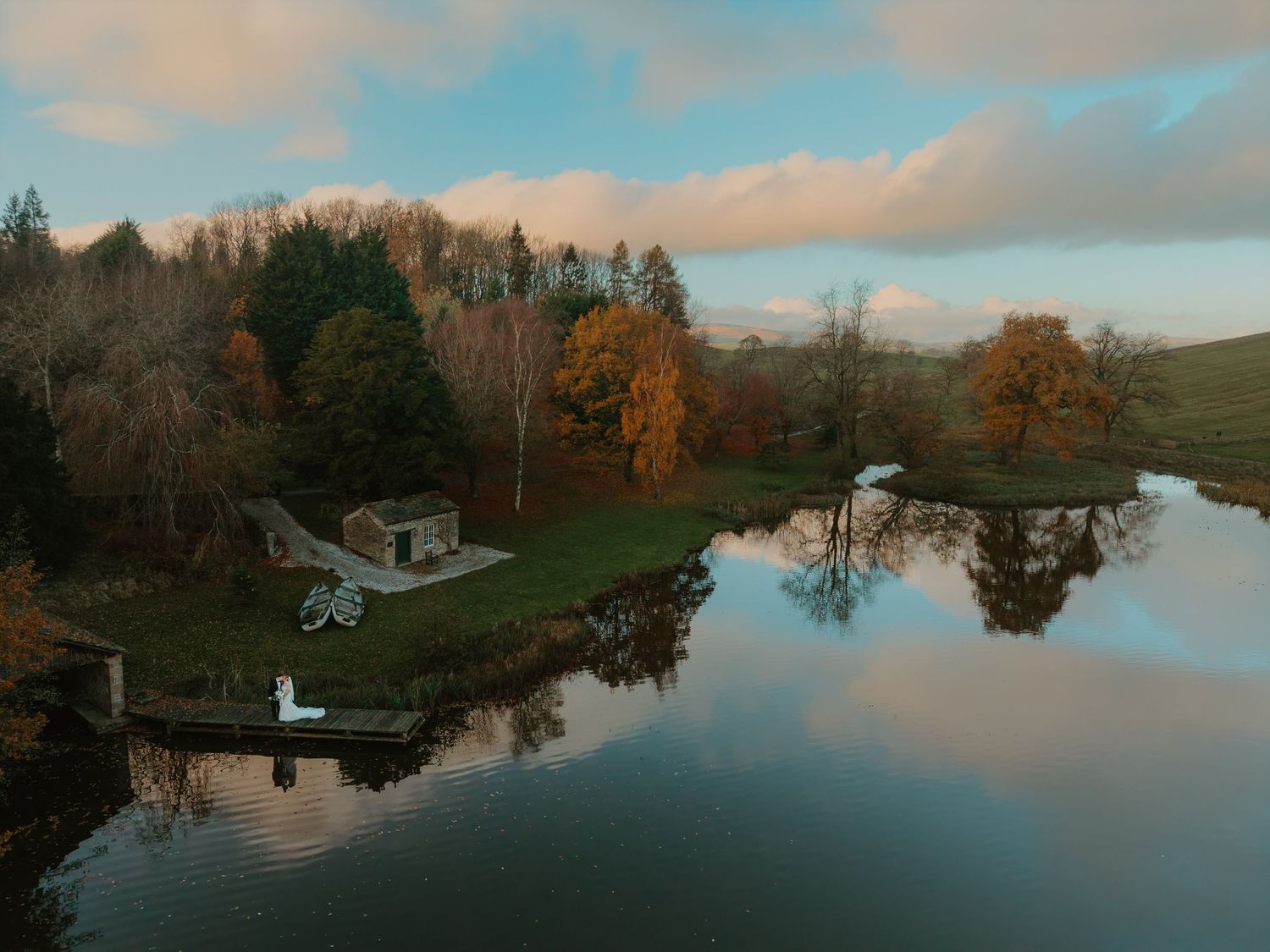 A serene waterway reflects autumn trees and cloudy skies with boats docked along the peaceful shoreline.
