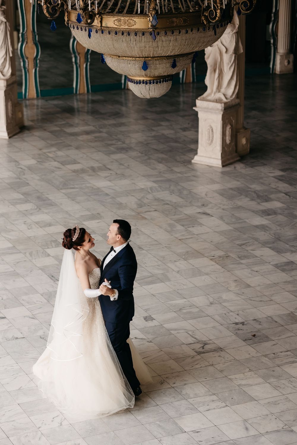 A romantic first dance sequence between newlyweds in a grand ballroom with ornate decor and marble floors.
