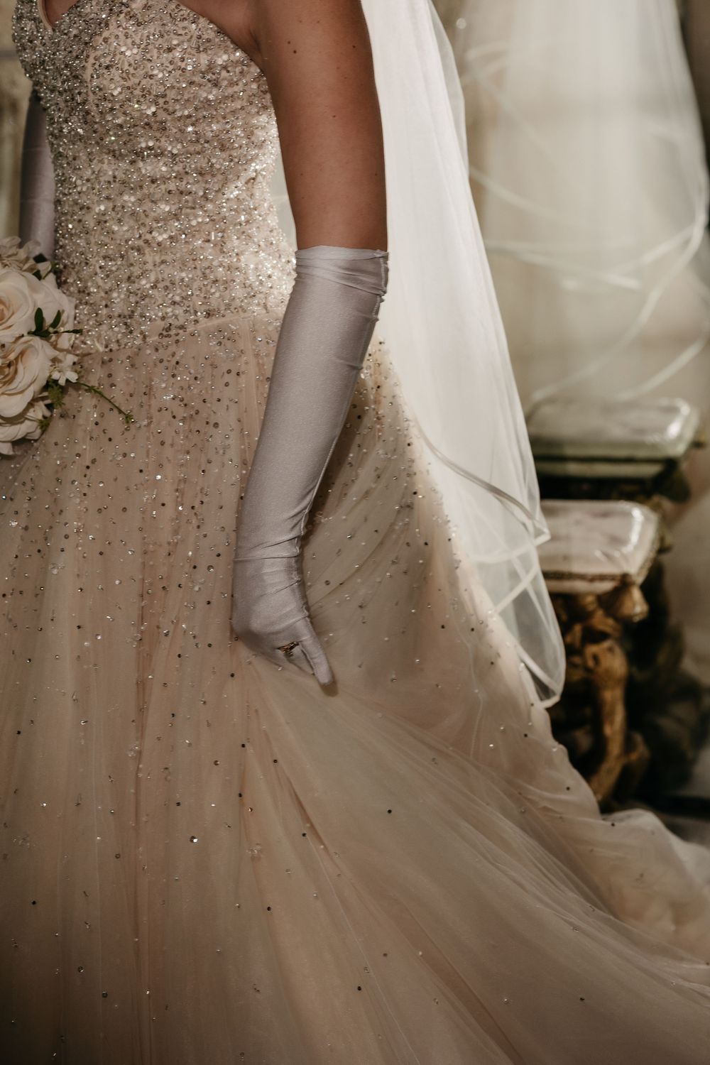 Close-up details of a white wedding dress with sparkling beaded embellishments and long satin gloves.
