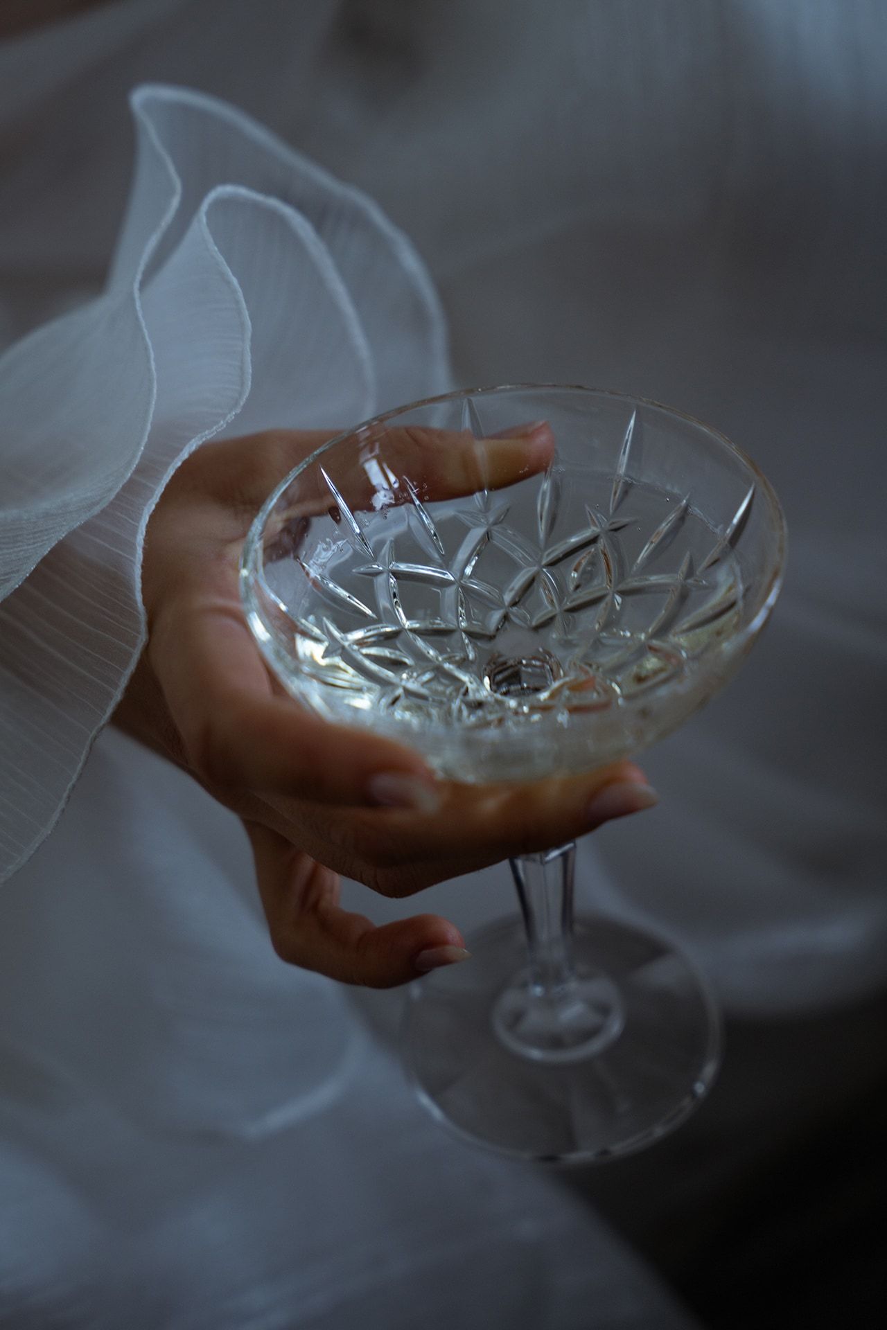 Crystal cocktail glass held in hands with soft, dreamy lighting effects.