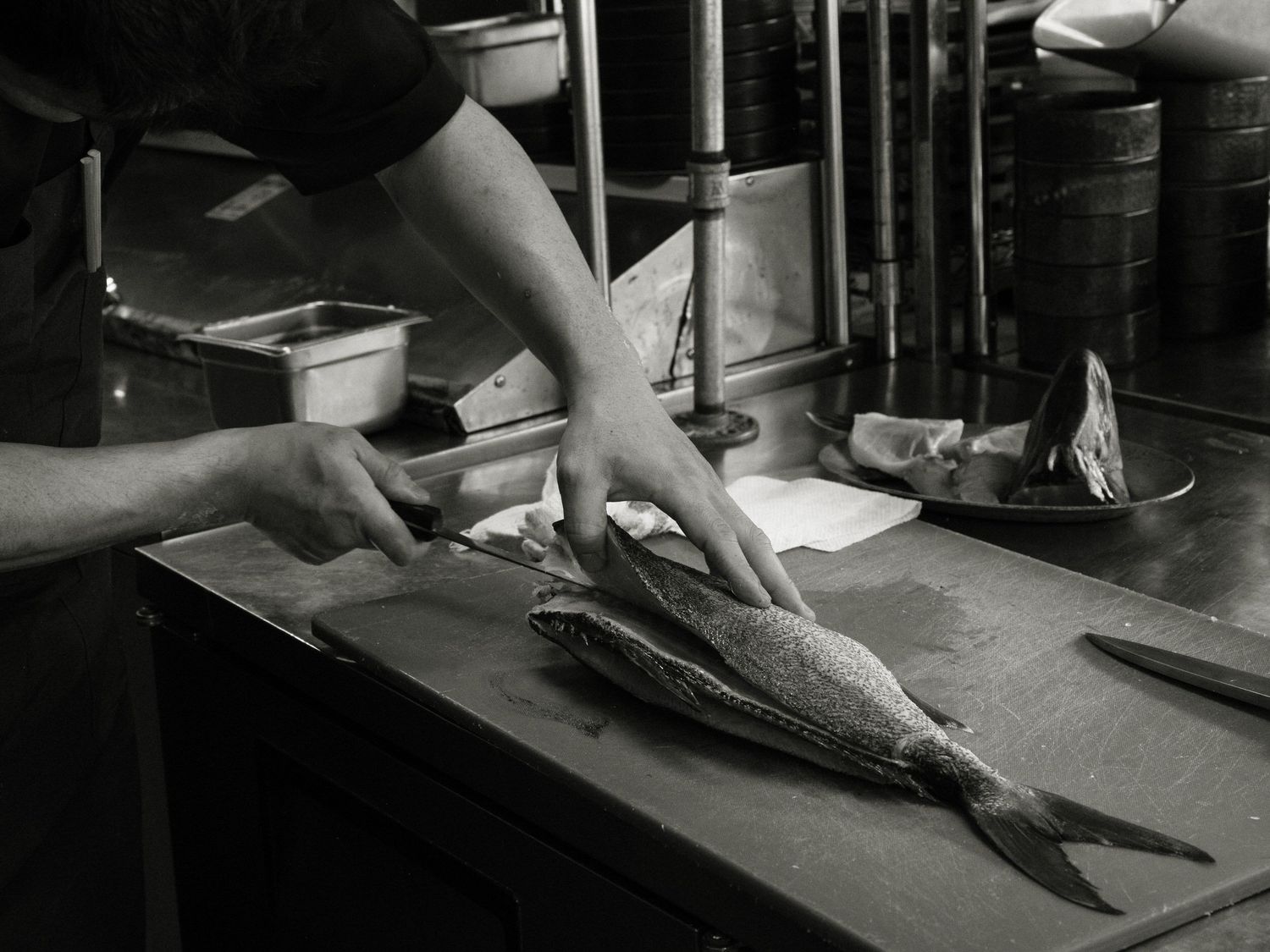 Chef slicing fresh fish on a blue cutting board in a dimly lit professional kitchen.