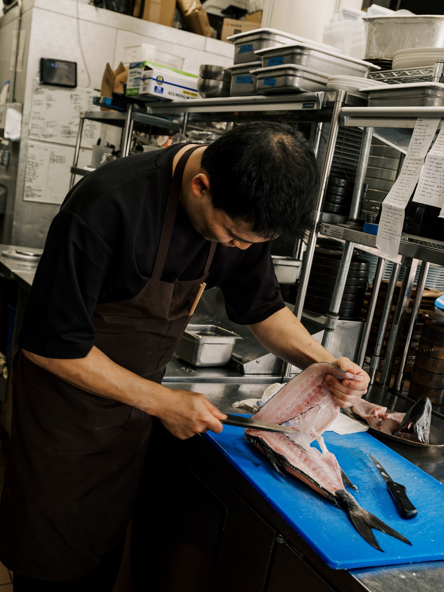 Chef fillets fish on blue cutting board in professional kitchen setting.