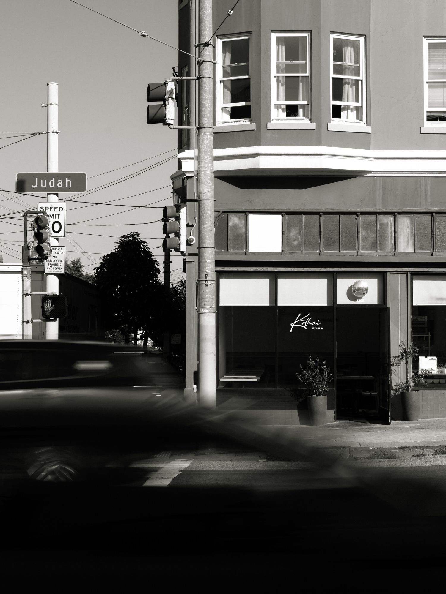 Black and white urban street scene with storefronts and utility poles.