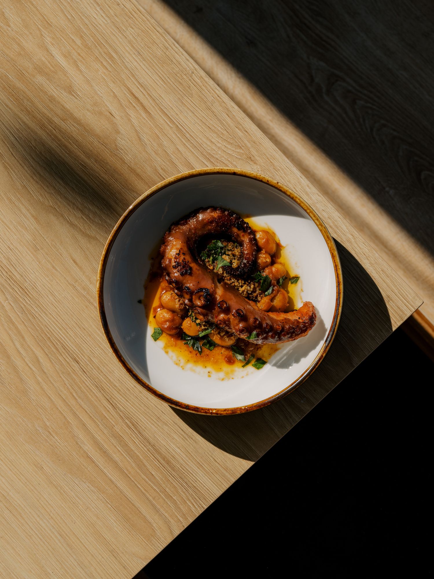 Grilled octopus tentacles served on a white plate with orange sauce and fresh herbs in dramatic lighting.