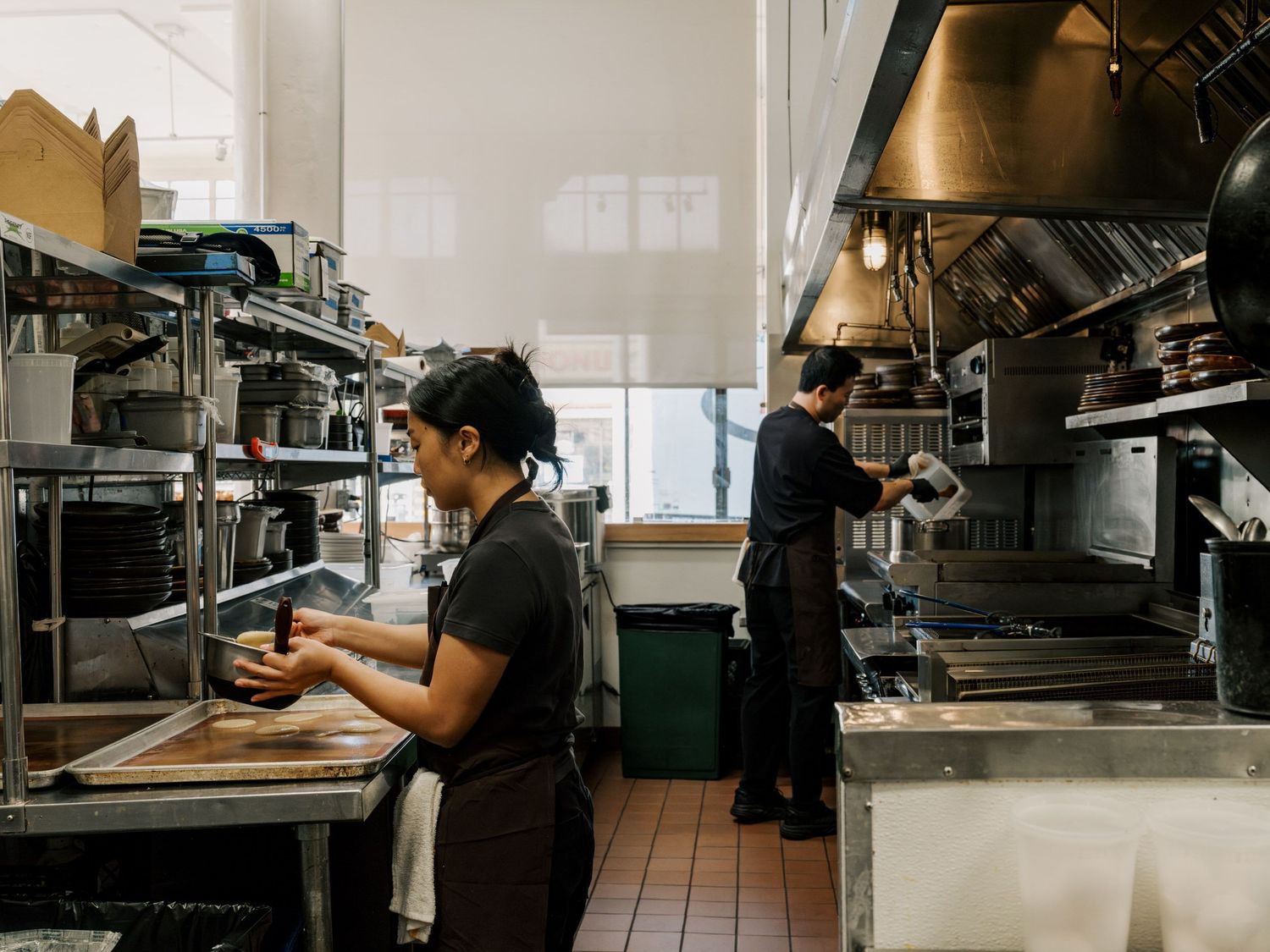 Restaurant kitchen staff working at cooking stations with industrial equipment and stainless steel appliances.