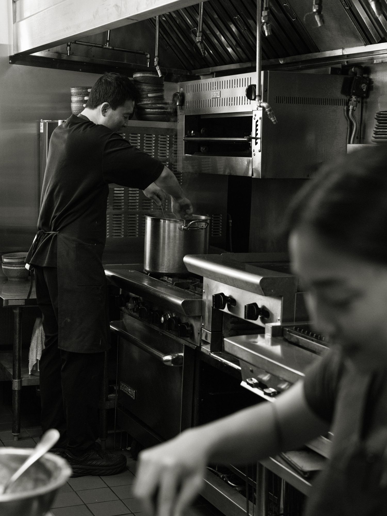 Black and white photograph showing the interior of a commercial kitchen with stainless steel equipment and appliances.