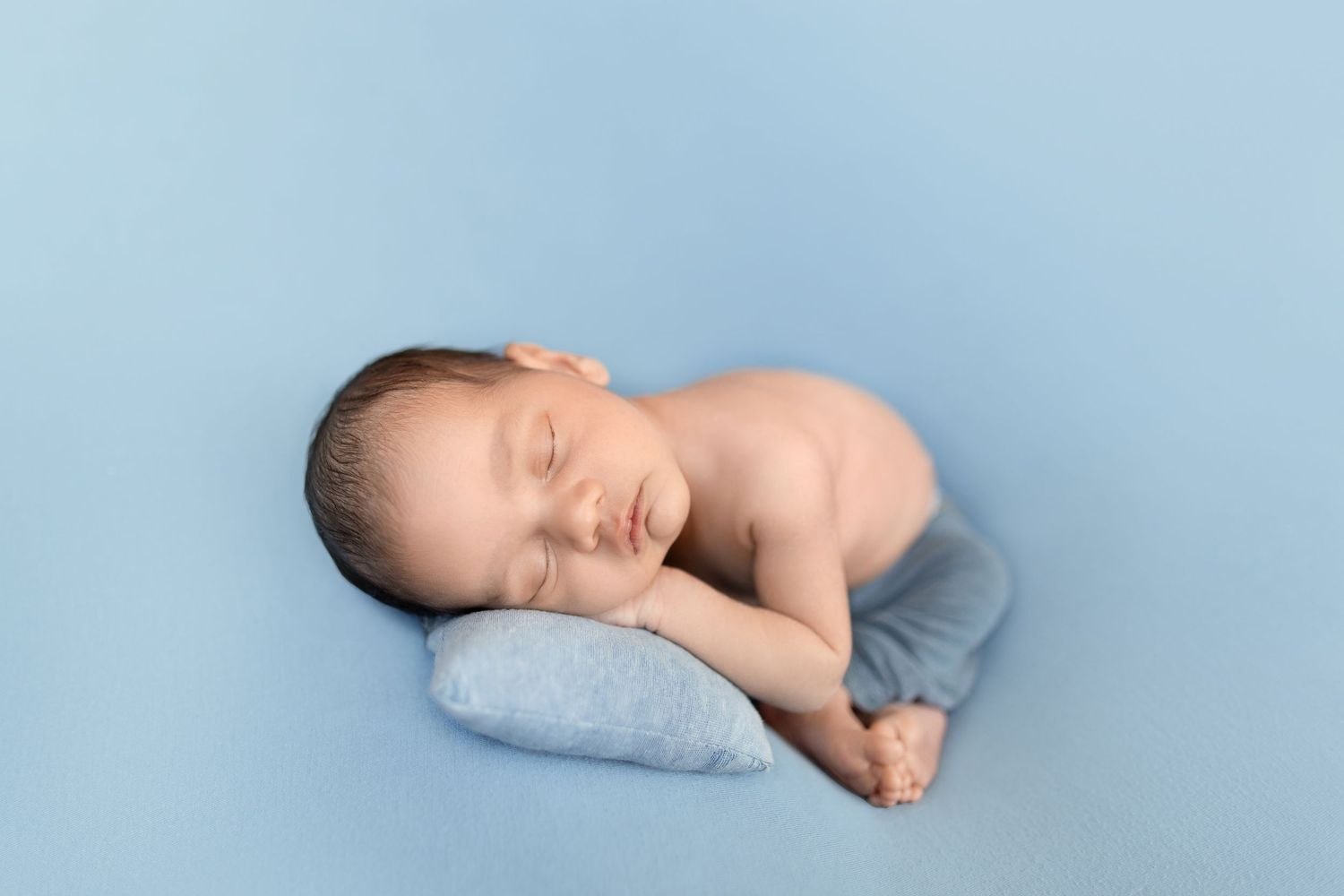 Sleeping newborn baby wrapped in light blue blanket on soft blue background in multiple poses.