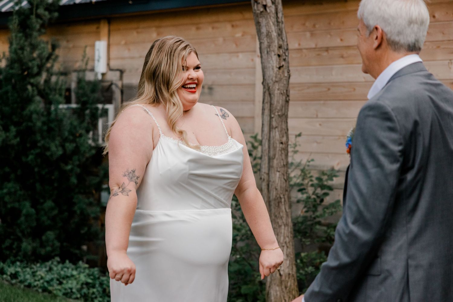 A joyful moment shared between a bride in a white dress and someone in a grey suit during an outdoor wedding.