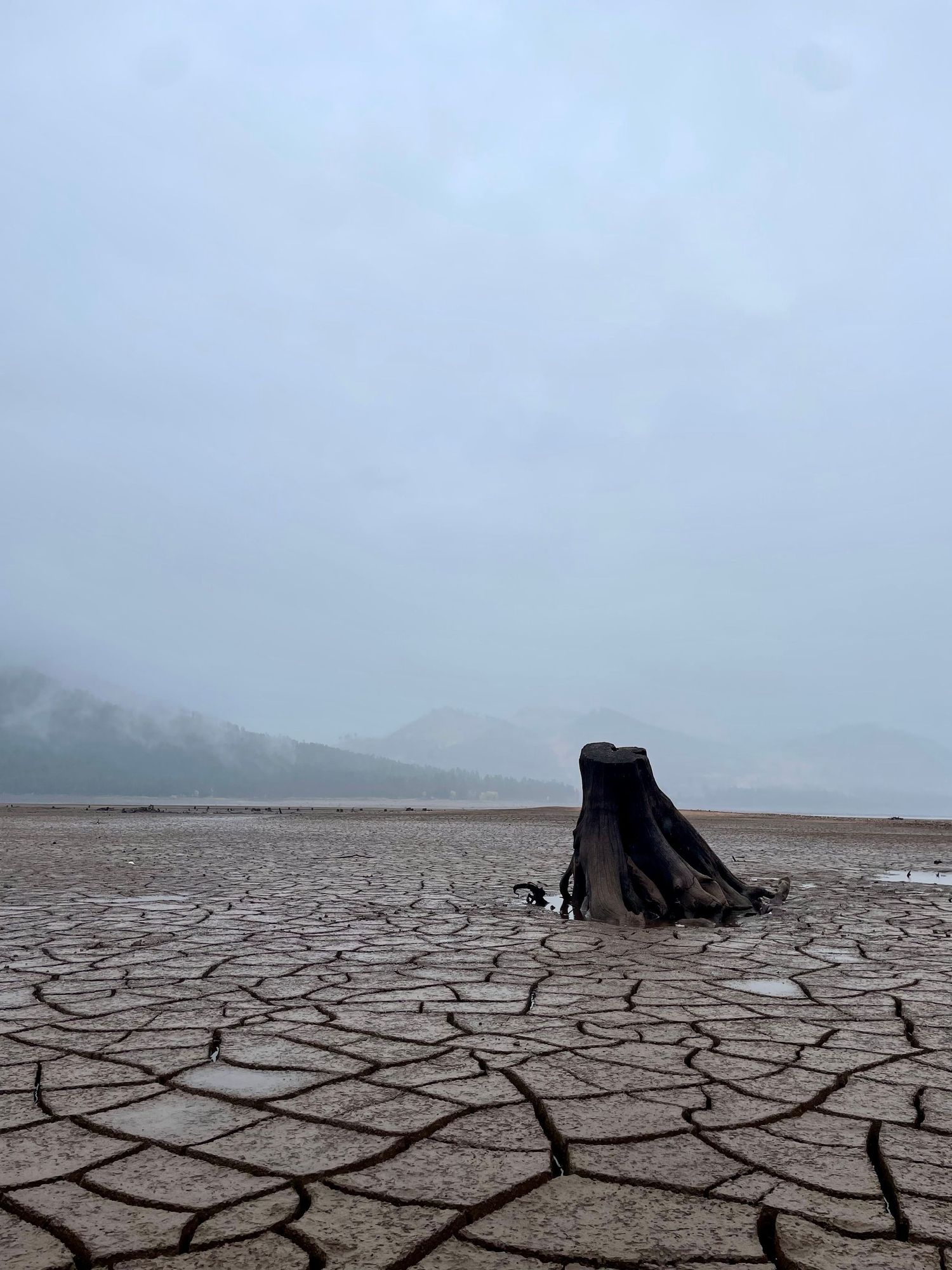 Cracked dry earth and distant mountains reveal a desolate drought-stricken landscape with dark figures in the distance.