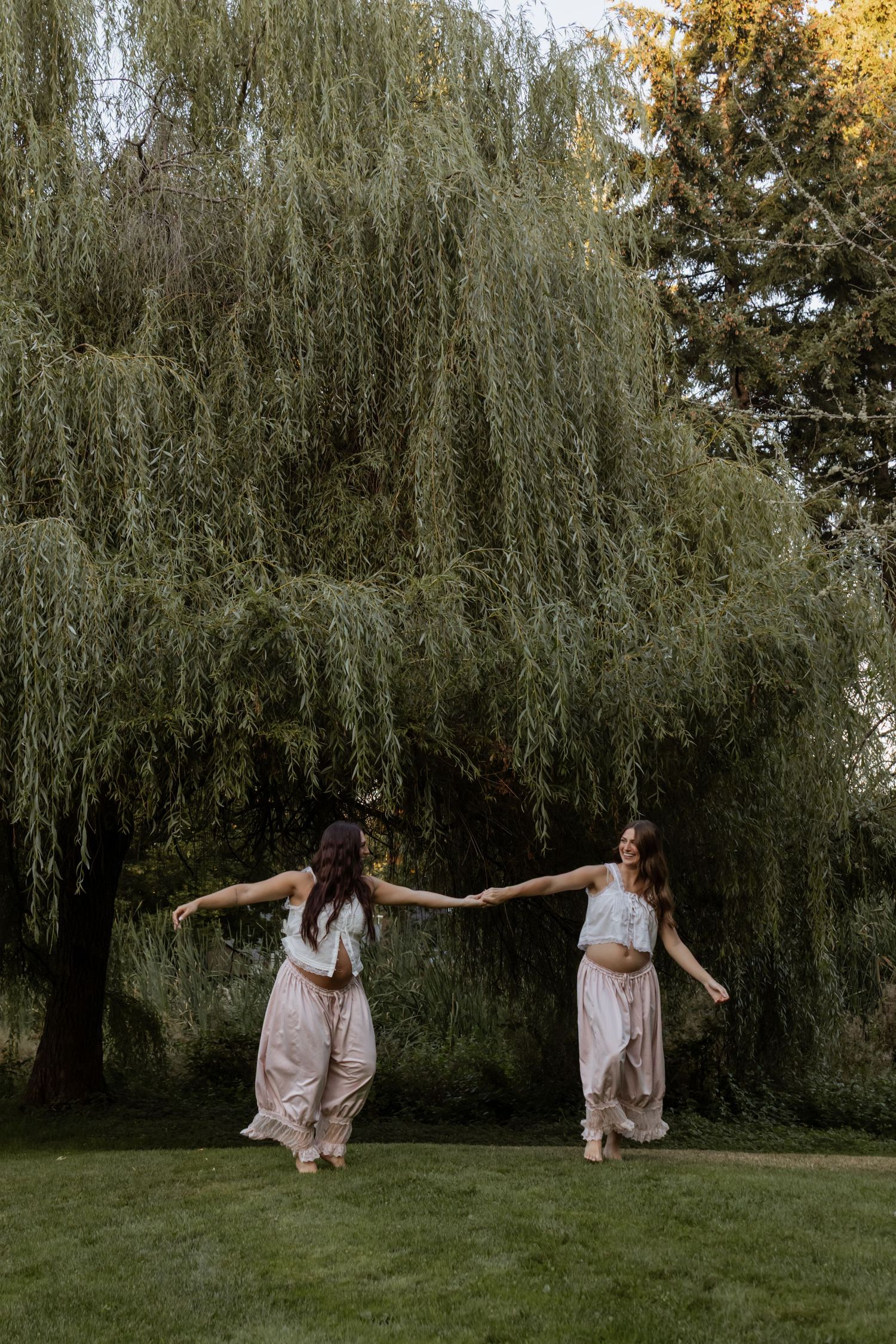 A couple in rustic western outfits dance joyfully in a field surrounded by vibrant yellow and green autumn trees.