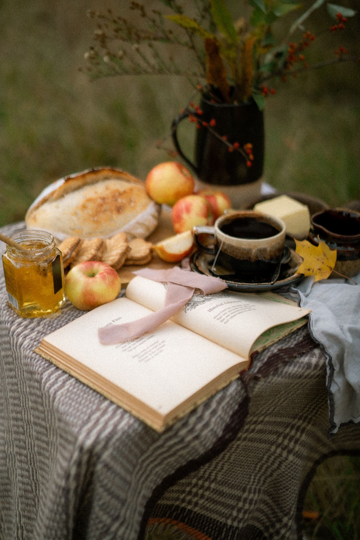 A cozy still life scene with an open book, apples, honey, and tea arranged on a gray striped fabric.