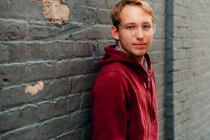 A person in a burgundy hoodie stands against a textured concrete wall in a series of connected photos.