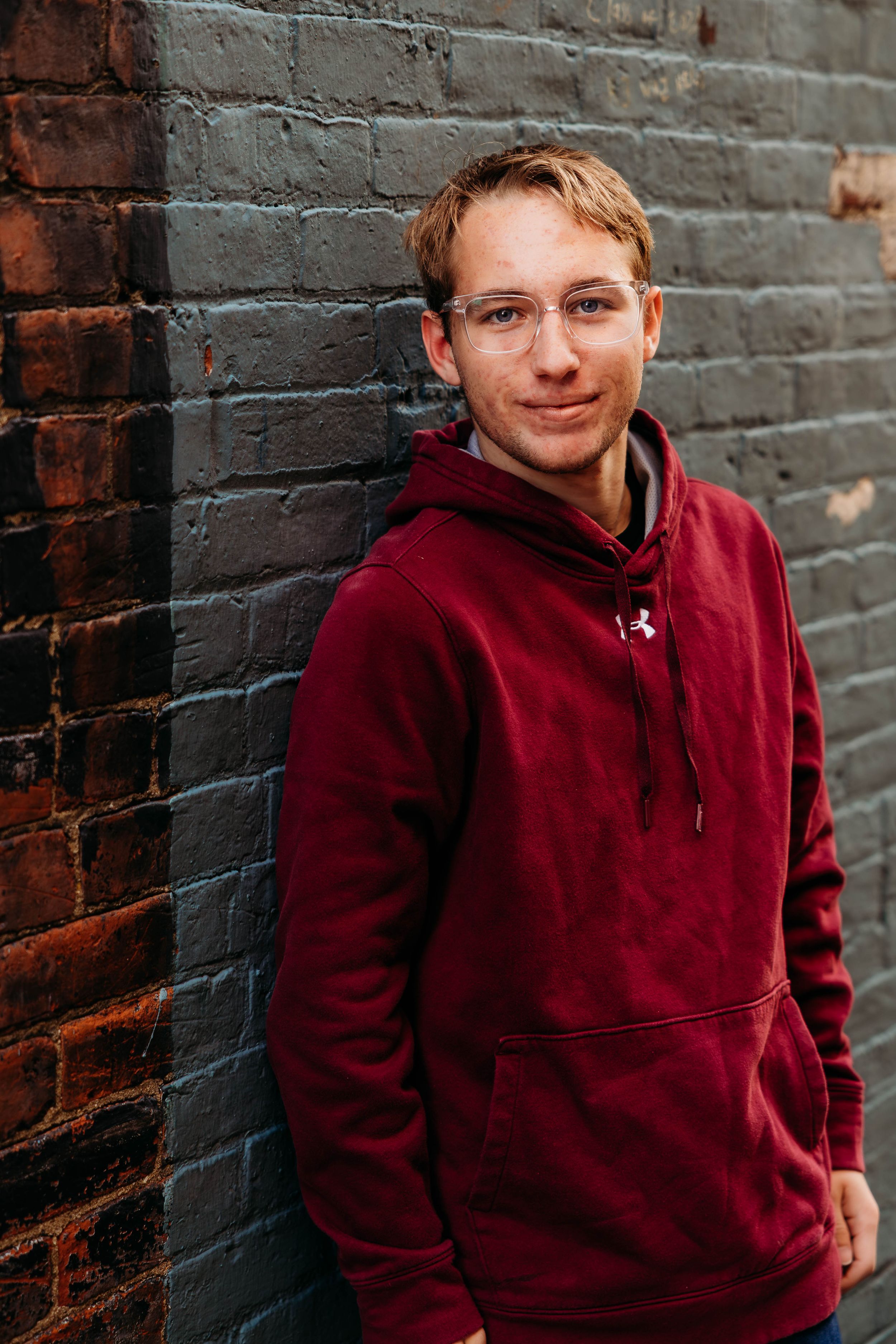 A series of casual portrait photos against a brick wall showing someone wearing a burgundy Under Armour hoodie.
