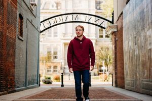 A person in a burgundy sweater walks through an arched brick passageway on a bright autumn day.