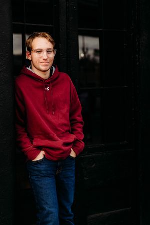 A person in a burgundy hoodie and blue jeans poses casually against a dark background in a series of photos.