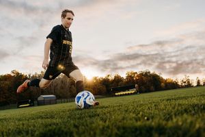 Soccer player kicking a ball on a grassy field at sunset with golden light illuminating the scene.