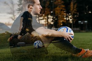 Soccer player in action making a diving save on grass field during autumn sunset.