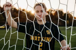 Soccer players celebrate near a goal net during an intense match wearing black and yellow uniforms.