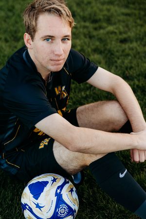 A soccer ball rests on green grass next to someone wearing a dark athletic uniform.