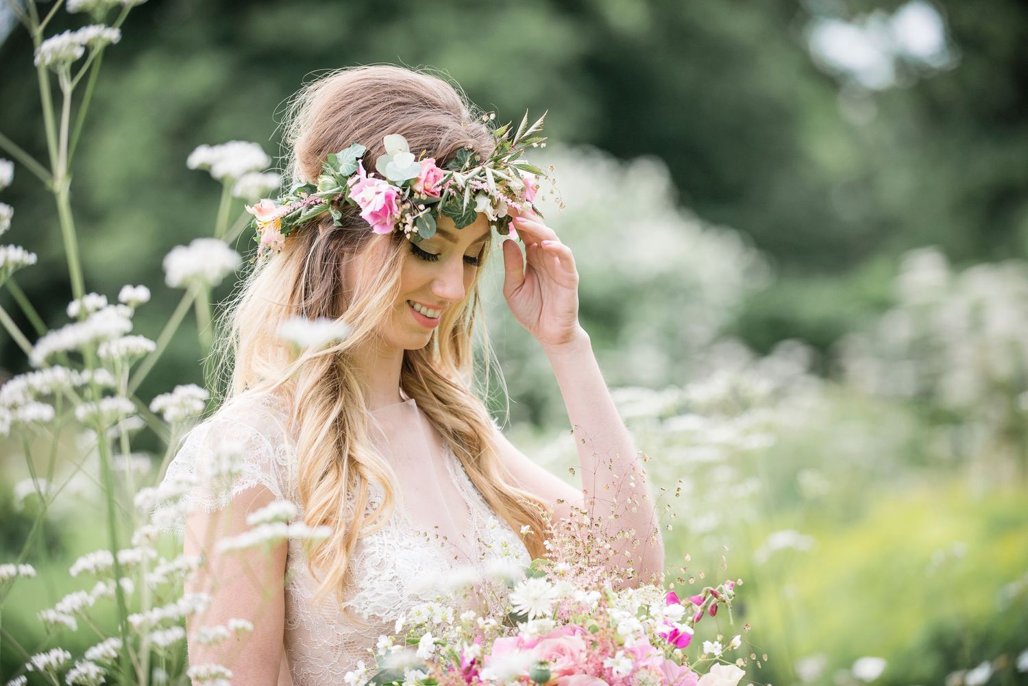 A person wearing a floral crown poses in a dreamy meadow filled with white wildflowers and tall grass.
