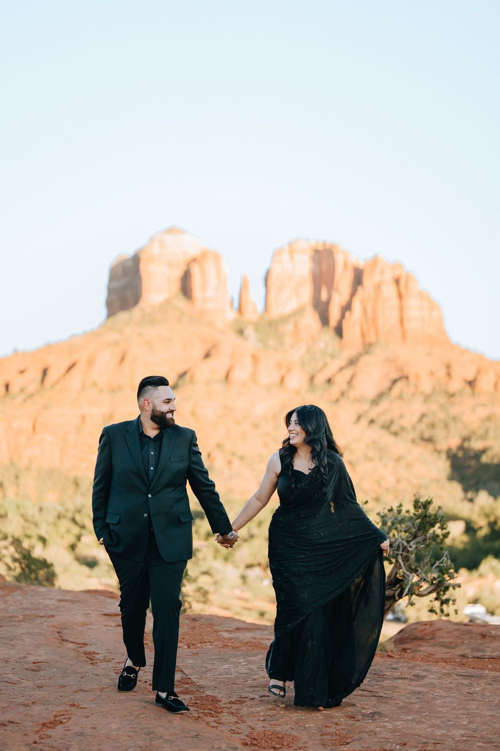 Couple in black attire posing against majestic red rock formations in desert landscape.