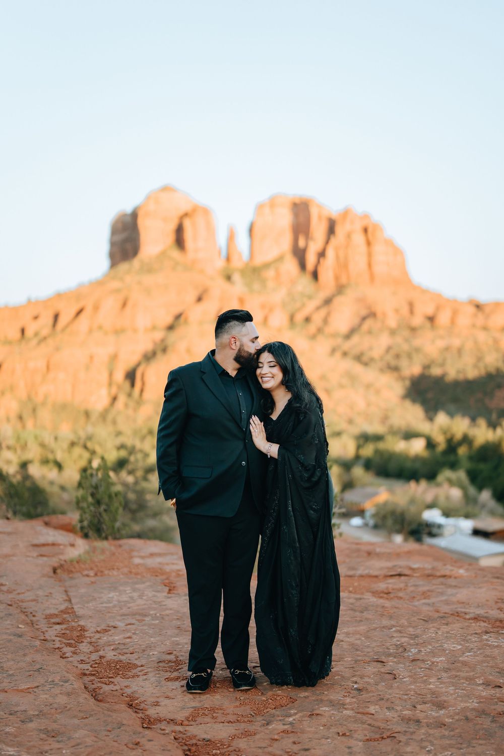 Intimate moment captured between two people on red rocks with majestic desert mountains in the background.