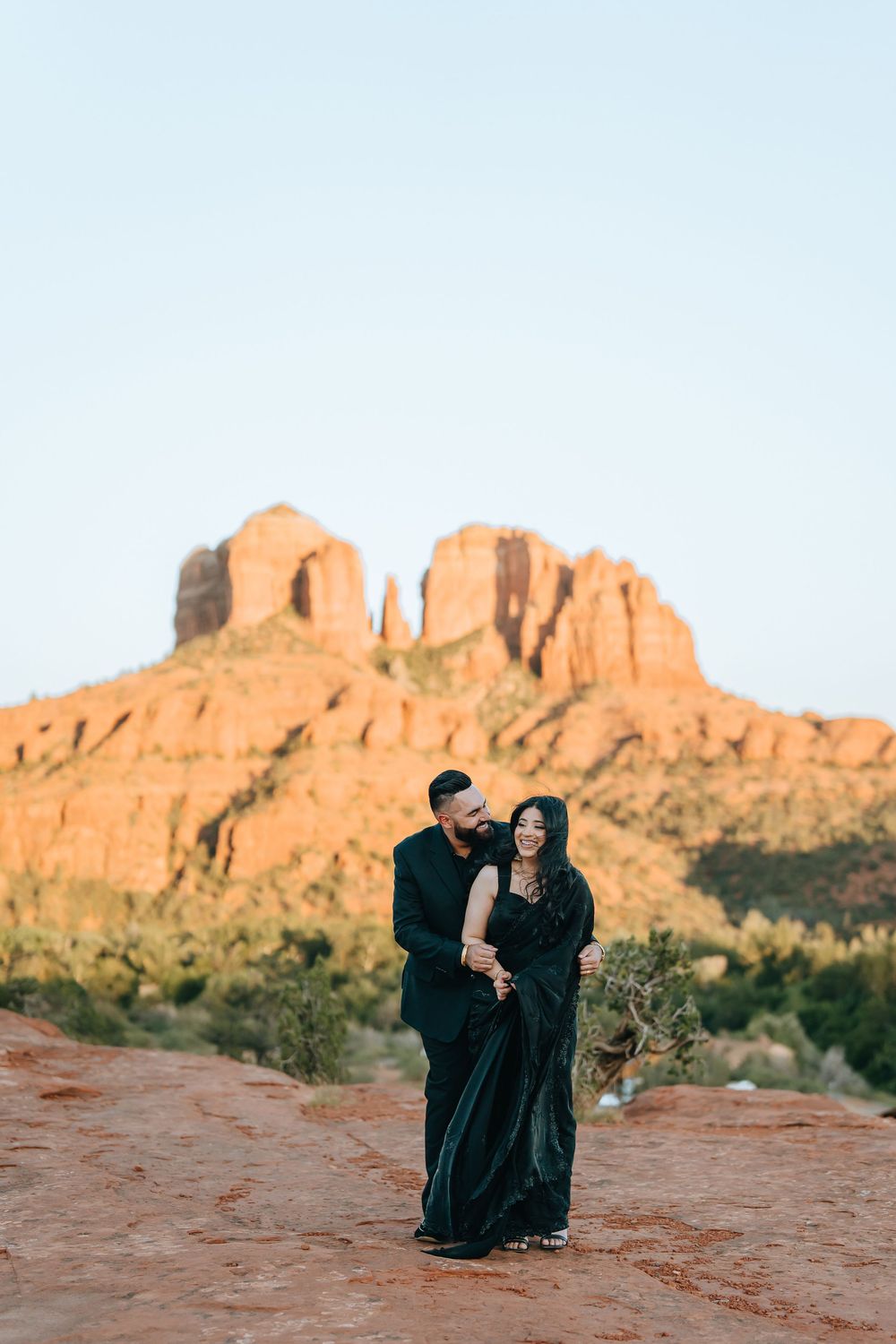 Romantic desert photoshoot with two people in black against dramatic red rock formations.
