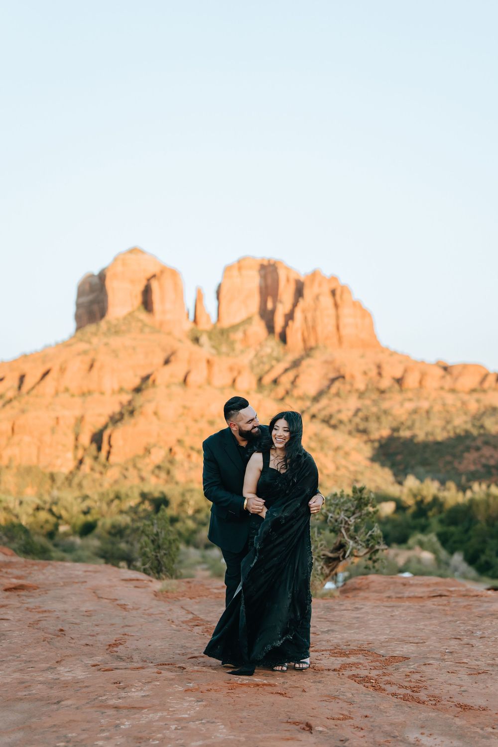 Couple dressed in black sharing intimate moments on red desert rocks with mountain backdrop.