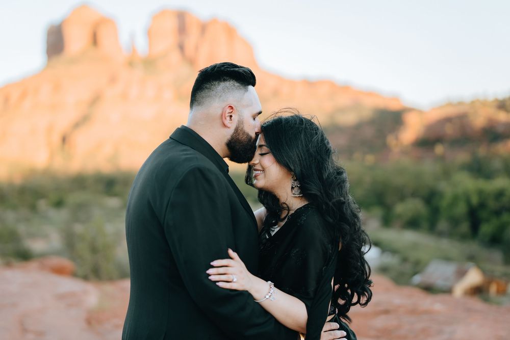 Intimate desert photo session featuring two people in black against red rock cliffs.