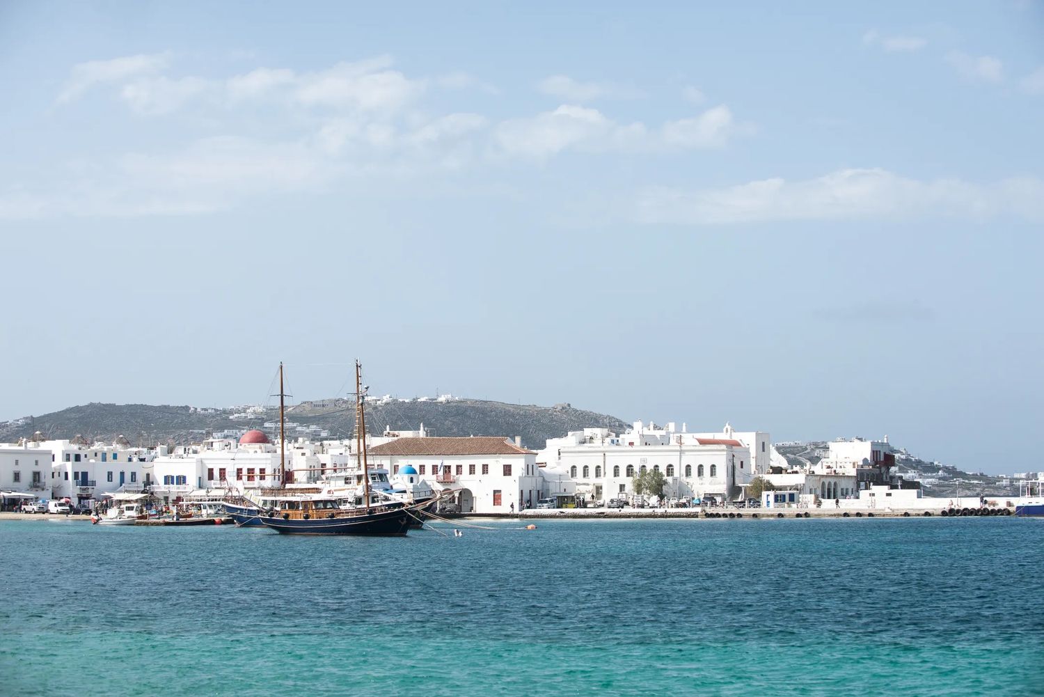 A coastal Greek harbour with boats and white buildings across clear turquoise water.