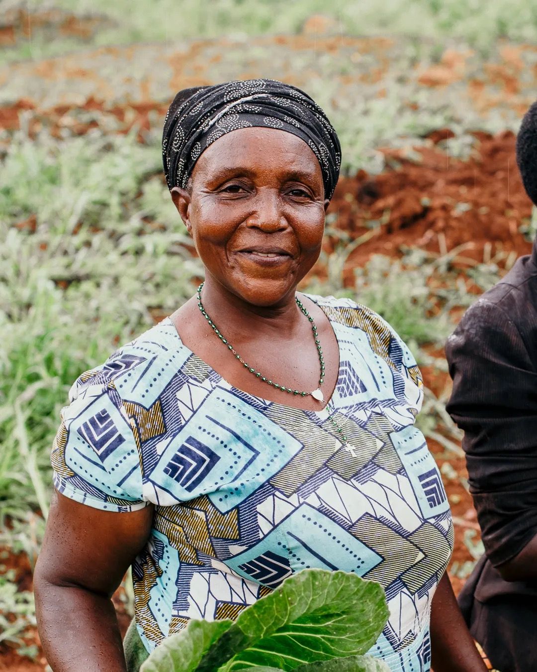 Smiling woman stands in a field, representing farming, confidence and community livelihood.
