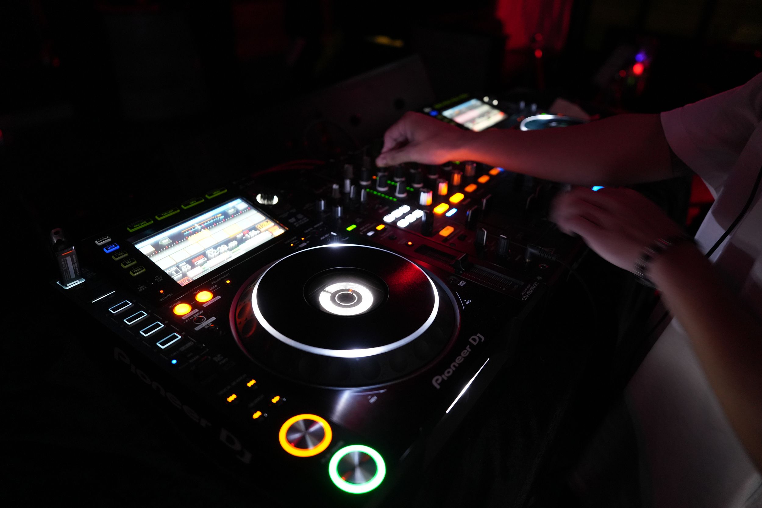 Professional DJ equipment with illuminated turntable and mixer controls being operated in a dark nightclub setting.