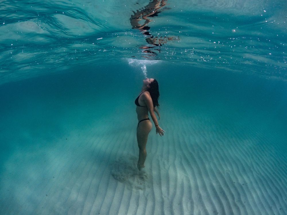 Underwater sequence showing swimmers floating in shallow turquoise waters with sandy bottom visible.