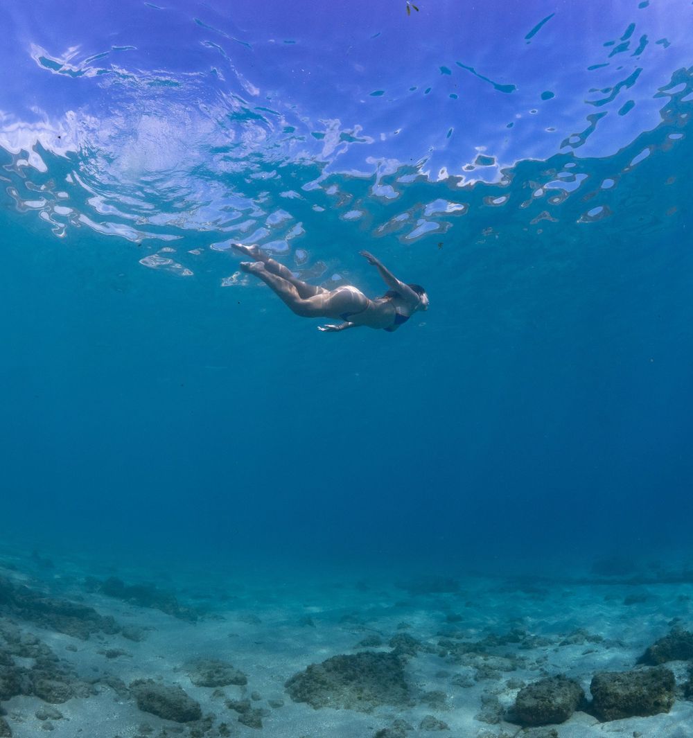 Underwater view of a swimmer gliding through crystal clear turquoise waters above a coral reef.