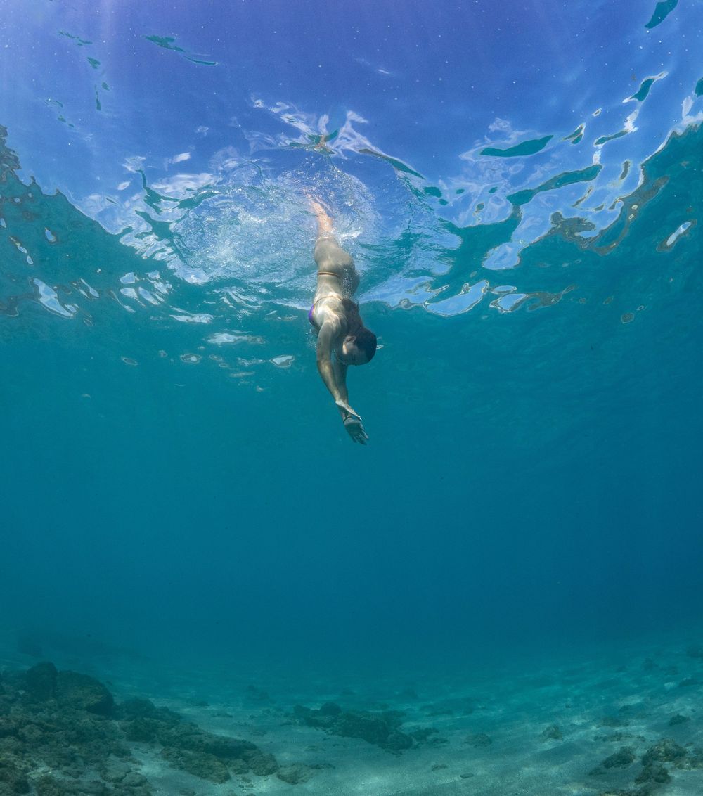 Swimmer diving beneath turquoise waters with sunlight streaming through the surface.