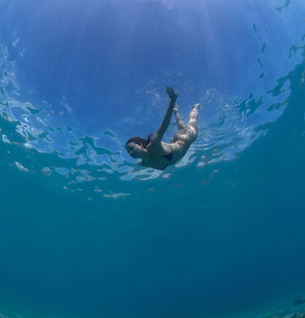 Underwater view of a swimmer diving deep in clear blue tropical waters with sunlight filtering through.