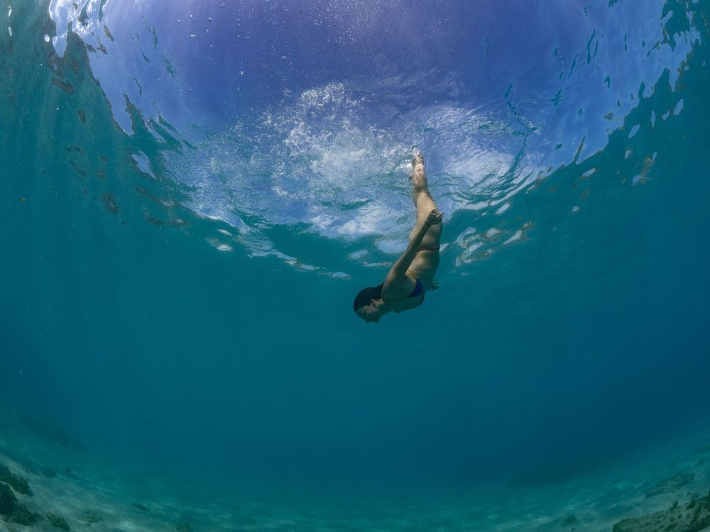 Underwater perspective of a swimmer floating beneath the surface of turquoise waters.