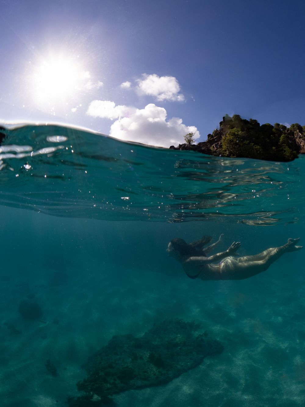 Underwater split shot of a sea turtle swimming near the ocean surface with sunlight streaming through turquoise waters.