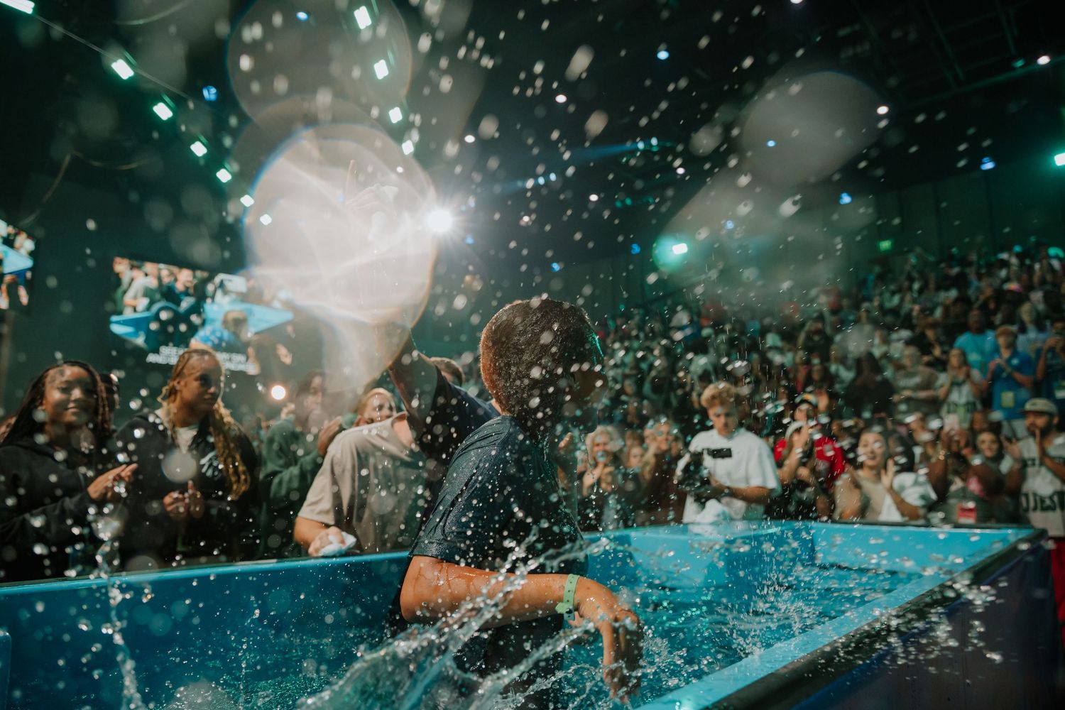 Dynamic splash captured mid-baptism as a person is immersed in water before a large church congregation.