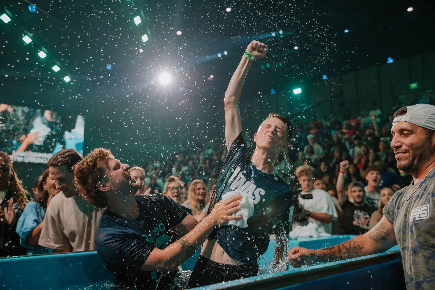 Excited young man celebrates after baptism in water tank before large church congregation audience.