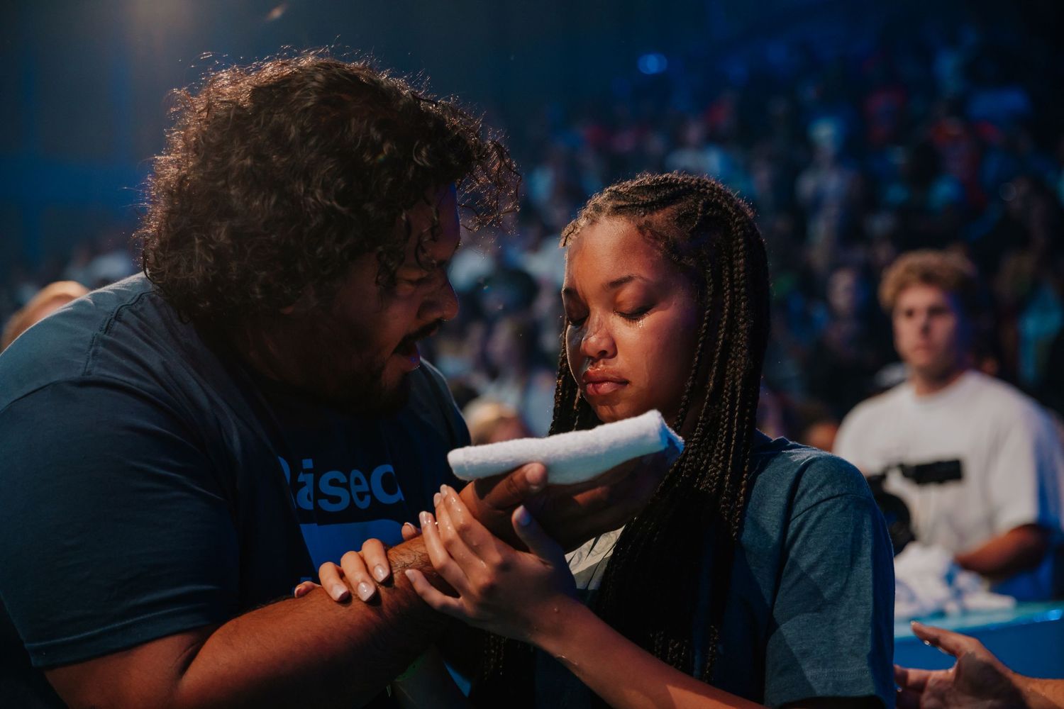 Pastor shares quiet moment reading scripture with young girl before baptism in dimly lit church.