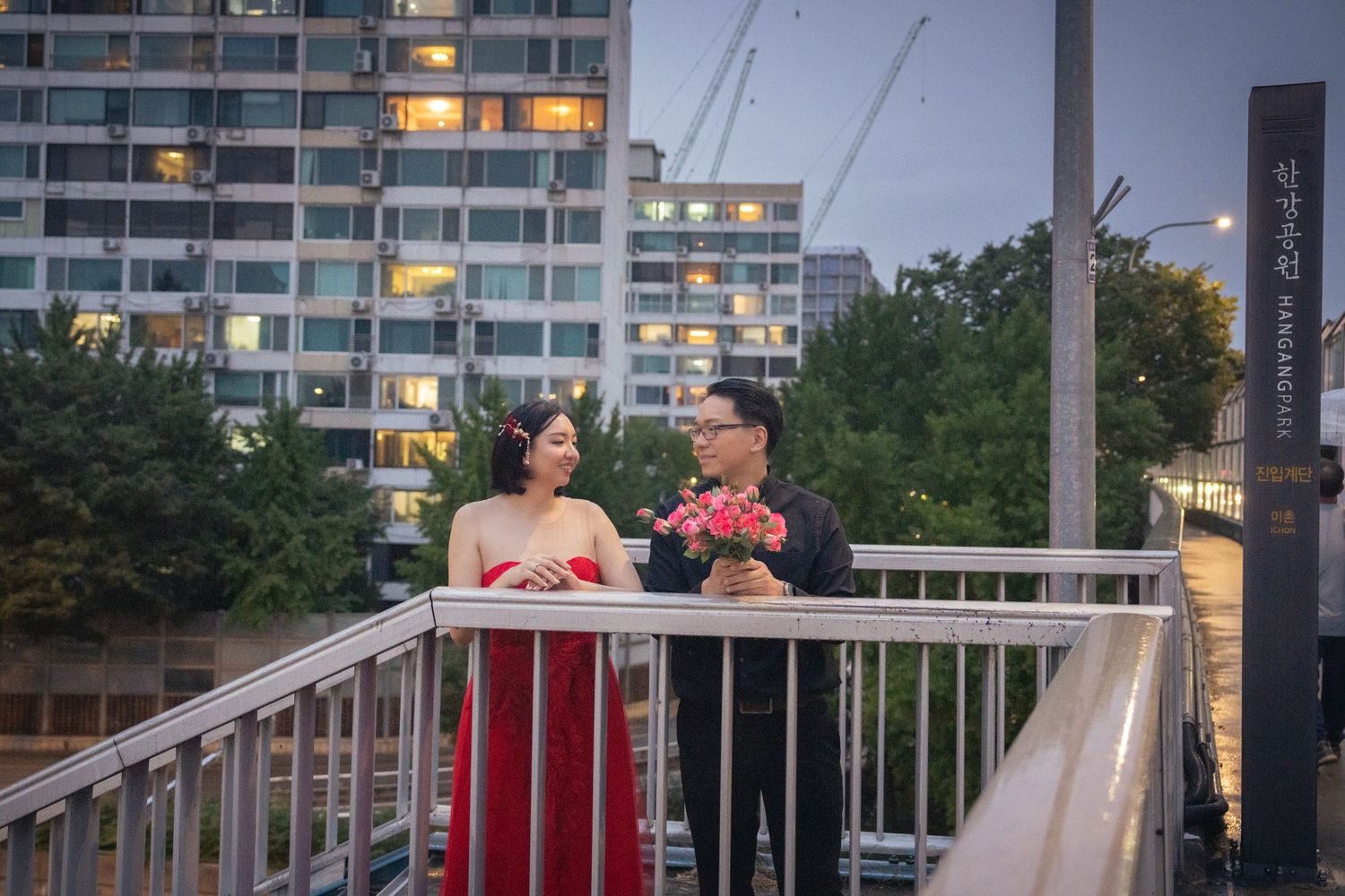 Couple in wedding attire sharing a joyful moment on a balcony with apartment buildings in the background.