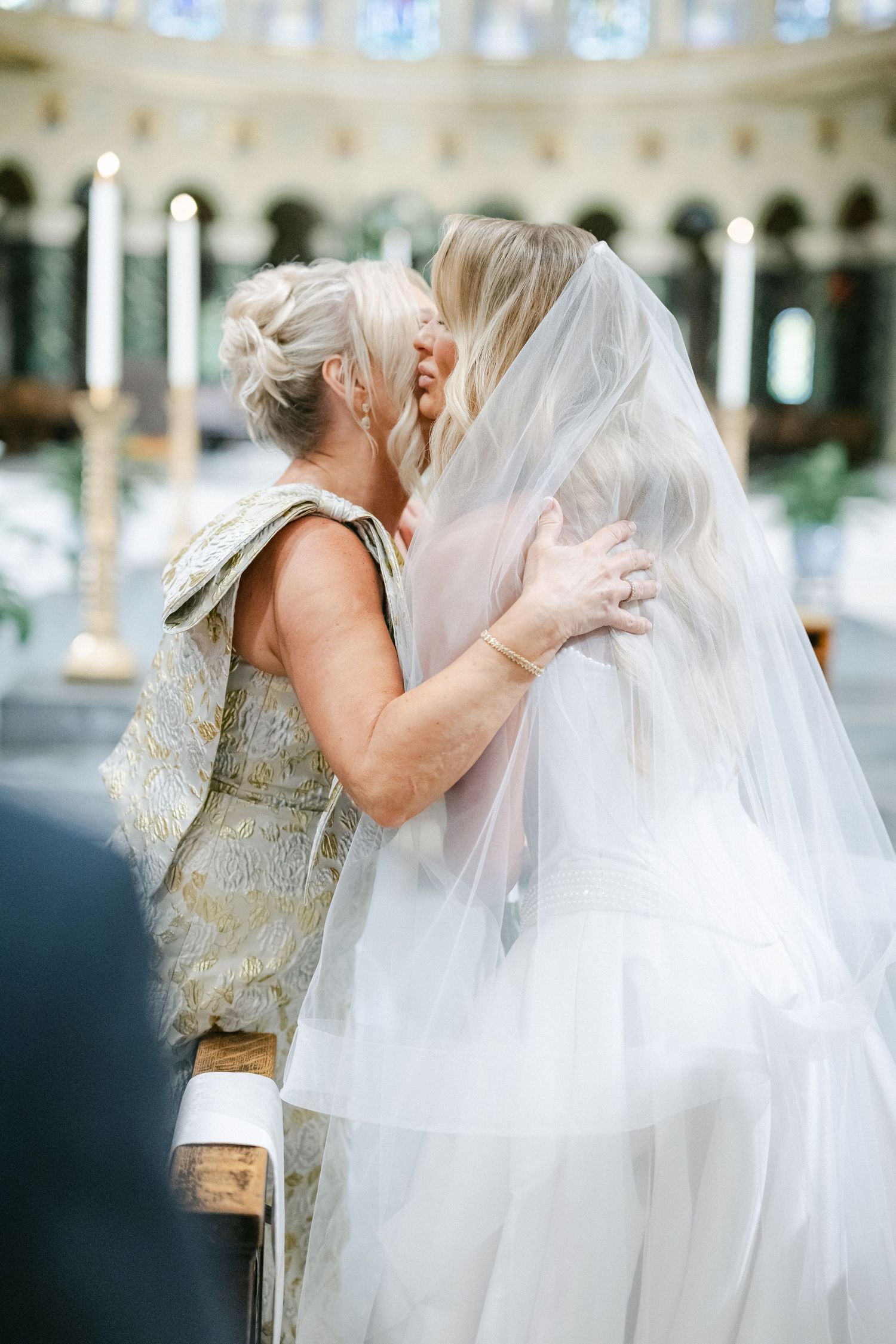 A tender moment shared between two people in formal attire with a flowing white veil at an elegant wedding venue.