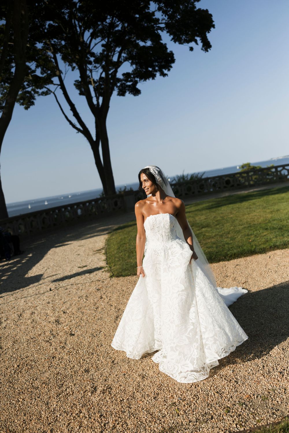 Radiant bride in strapless lace ball gown with cathedral veil walks along sunlit garden path.