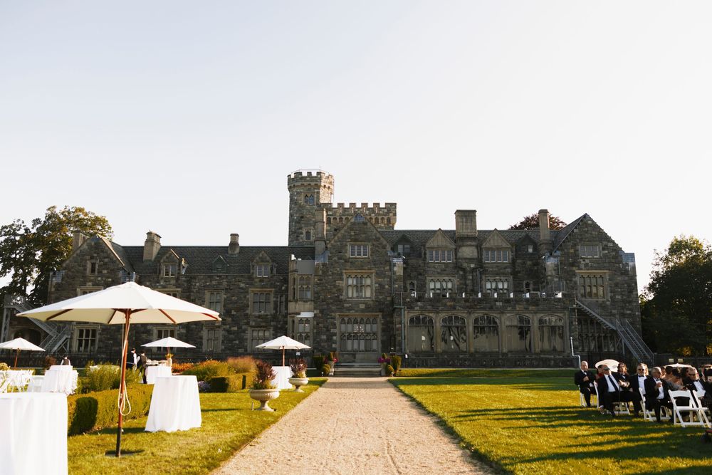 Grand stone castle estate serves as stunning outdoor wedding venue with manicured lawns and guests gathering for ceremony.